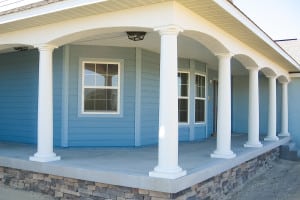 Blue exterior country-style home featuring a wrap-around porch, white columns, and dormer windows.