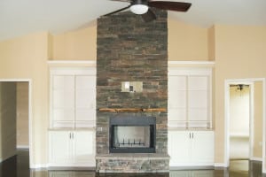 Living room interior featuring a stacked-stone fireplace, built-in cabinetry, and vaulted ceiling.