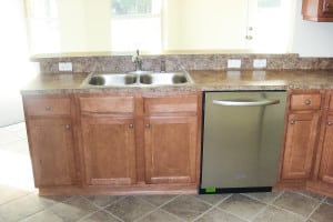 Kitchen sink area in a country-style home featuring wood cabinets, tile backsplash, and stainless steel dishwasher.