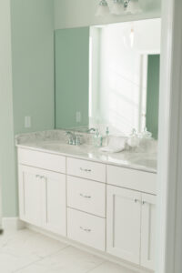 Farmhouse bathroom vanity with white cabinetry, marble countertops, and soft green walls