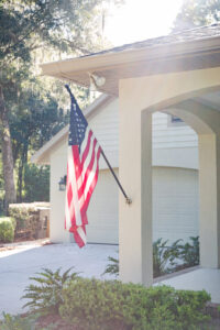 Covered front porch with American flag and arched columns on custom home