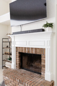 Brick fireplace with white mantel and mounted TV in custom home living room