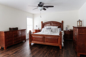 Spacious bedroom with wood flooring, ceiling fan, and natural light in custom home