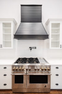 black range hood over gas stove with white cabinetry farmhouse kitchen