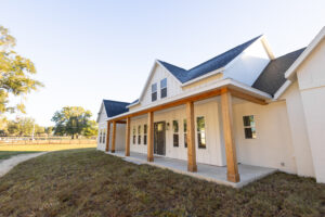 Two-story white board-and-batten custom farmhouse with wrap-around porch and cedar posts built by Curington Homes in Morriston, FL