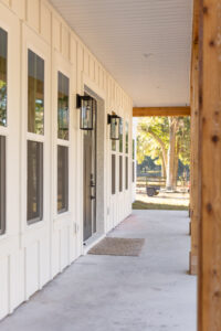 Covered farmhouse porch with cedar columns and black lantern sconces at a Curington Homes custom build in Morriston, FL