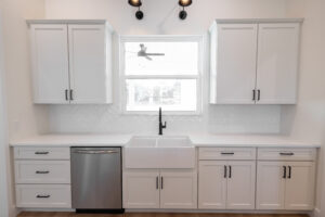 Farmhouse kitchen with white shaker cabinets, apron sink, matte black fixtures, and herringbone tile backsplash in a Morriston, FL custom home