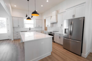 Open-concept farmhouse kitchen with waterfall quartz island, shiplap vent hood, and stainless appliances in a Morriston, FL custom home