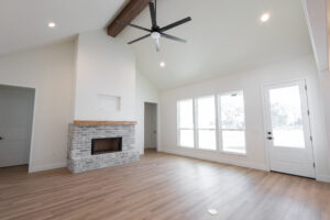 Vaulted great room with exposed wood beam, brick fireplace, and ceiling fan in a Morriston, FL custom farmhouse