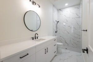 Bathroom with marble-look tile walk-in shower, floating vanity, and round black-framed mirror in a Morriston, FL custom farmhouse