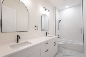 Guest bathroom with double vanity, arched black-framed mirrors, and tiled tub-shower combo in a Morriston, FL custom farmhouse