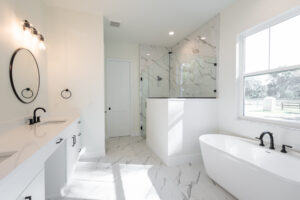 Primary bathroom with freestanding soaking tub, frameless glass shower, and marble-look tile in a Morriston, FL custom farmhouse
