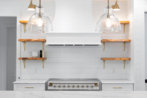 Modern farmhouse kitchen with stainless steel stove, vent hood, pendant lighting, and floating shelves in Morriston Florida