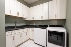 Custom laundry room with white cabinetry, countertop workspace, and stainless steel washer and dryer in Ocala Florida home