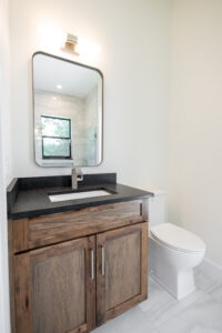 Custom bathroom vanity with wood cabinet, black countertop, modern mirror, and white toilet in Ocala Florida home