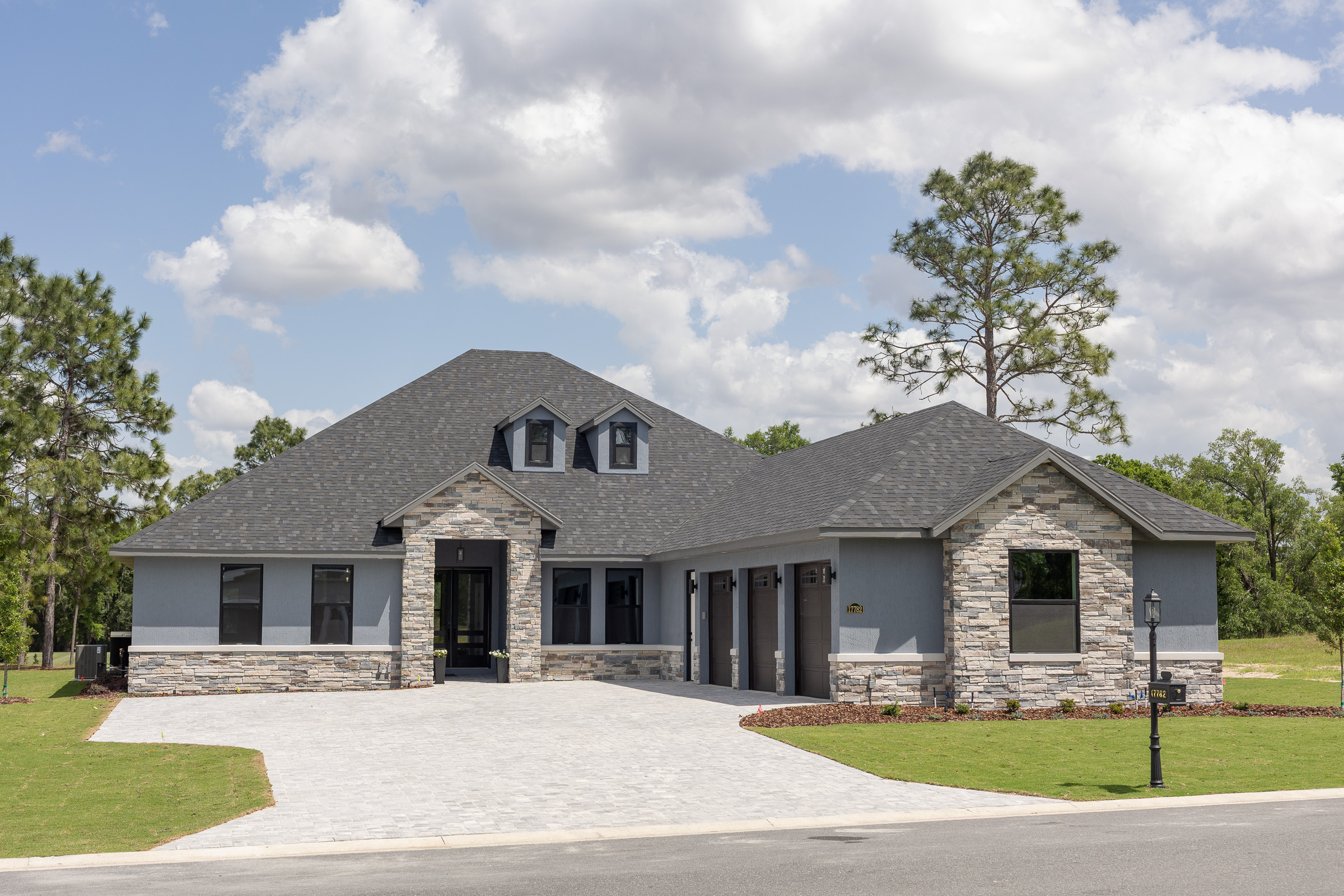 Modern gray custom home exterior with black trim windows, stone accents, and three-car garage in Dunnellon, Florida.