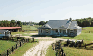 Farmhouse-style custom home with light exterior, black window frames, and a front porch surrounded by manicured landscaping.