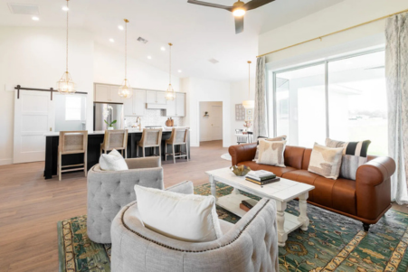 Open-concept living room and kitchen featuring modern lighting, leather sofa, and breakfast bar in a Curington Homes build in Ocala, FL