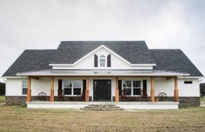 Front elevation of a custom-built country-style home featuring a deep front porch, dormer windows, and gabled roofing.