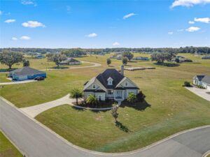 Aerial view of a custom country-style home situated on spacious acreage with surrounding landscape and driveways.
