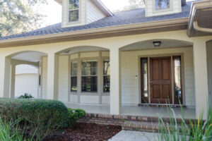 Front porch of a country-style home with decorative columns, brick steps, and a wooden entry door.